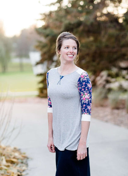 Woman wearing a raglan baseball style top. The shirt is gray with contrasting navy and pink floral sleeves.