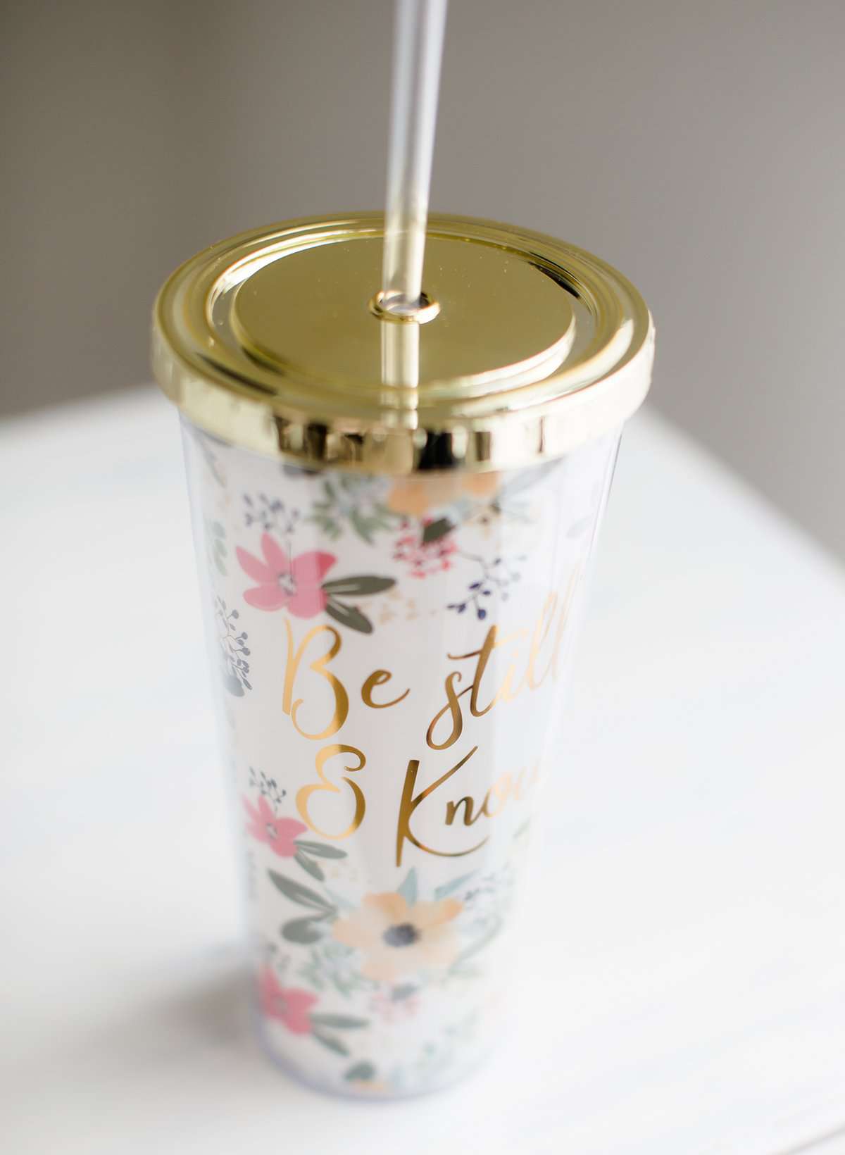 Be still and know double wall tumbler. This tumbler has flowers adorning it and accented with a gold cap and gold writing.