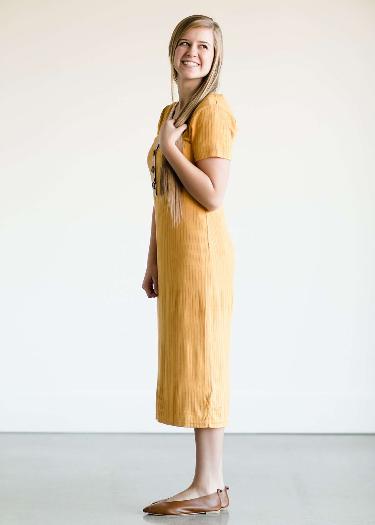 Woman wearing a ribbed mustard midi dress with faux wood buttons.