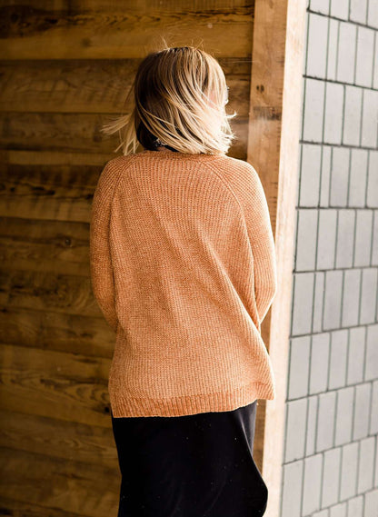 Woman wearing an open front cardigan that is chenille and camel in color. She is also wearing it over a black dress and brown riding boots. She is standing on the stairs at Inherit Clothing Company.