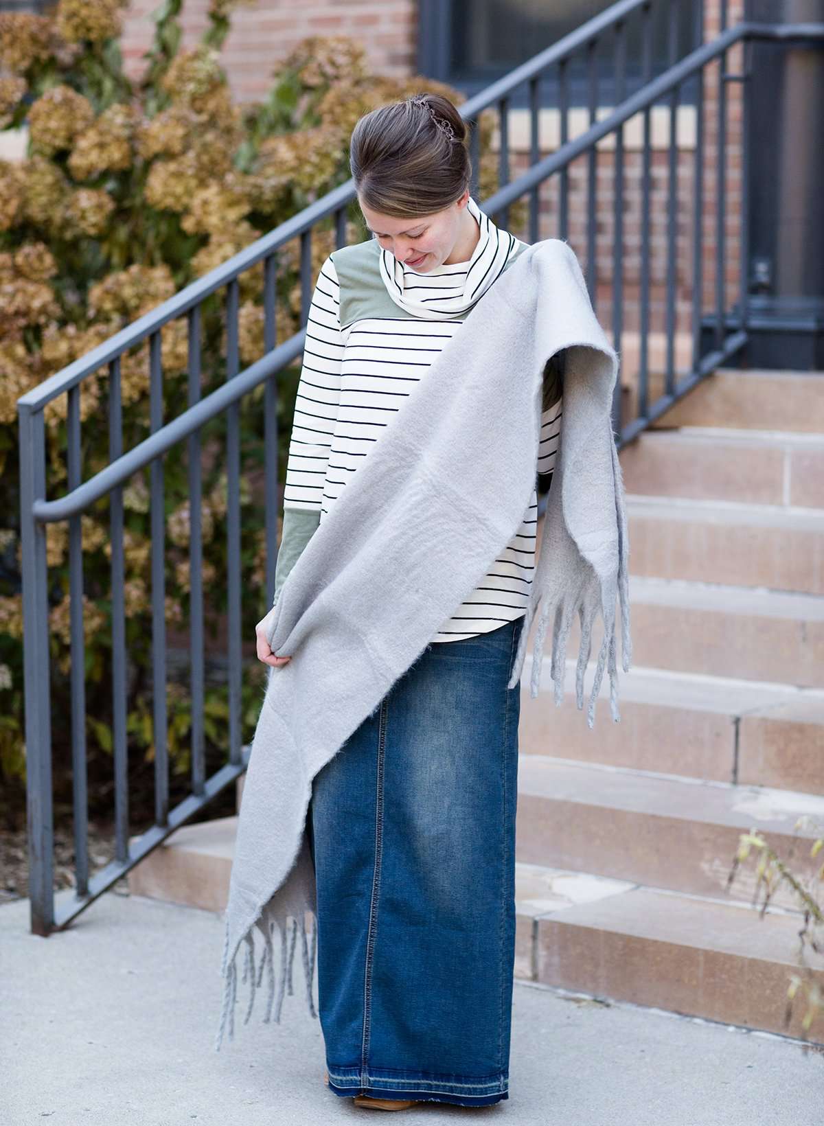 Woman wearing a gray fringe scarf that is super cozy and knit.