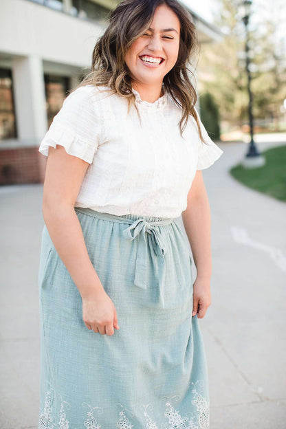 Woman wearing a mint green cotton midi skirt with a self tie and feminine crochet lace detail at the bottom hem