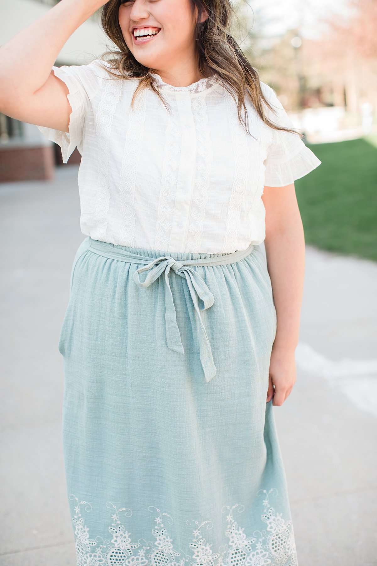 Woman wearing a mint green cotton midi skirt with a self tie and feminine crochet lace detail at the bottom hem