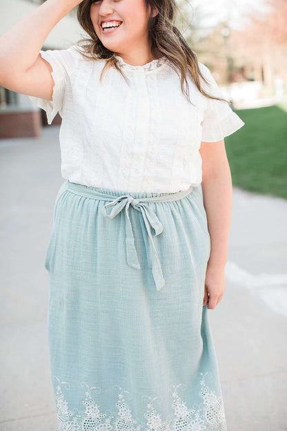 Woman wearing a mint green cotton midi skirt with a self tie and feminine crochet lace detail at the bottom hem