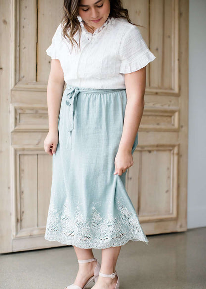 Woman wearing a mint green cotton midi skirt with a self tie and feminine crochet lace detail at the bottom hem