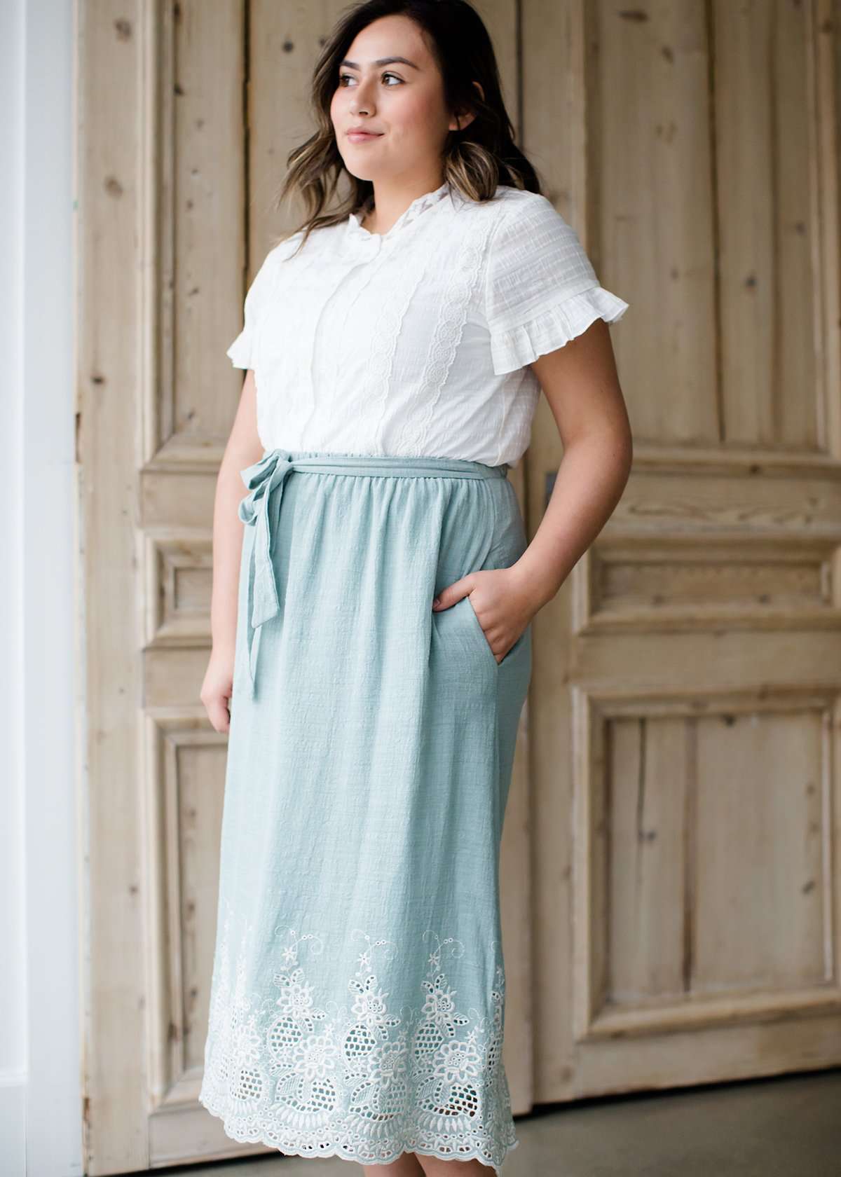 Woman wearing a mint green cotton midi skirt with a self tie and feminine crochet lace detail at the bottom hem