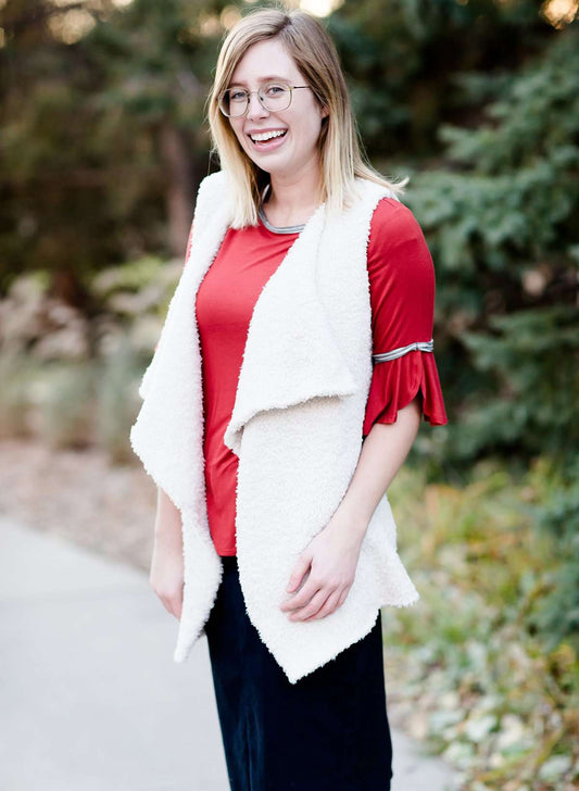 Young woman in a modest black midi skirt wearing a cream colored, soft drape style vest.