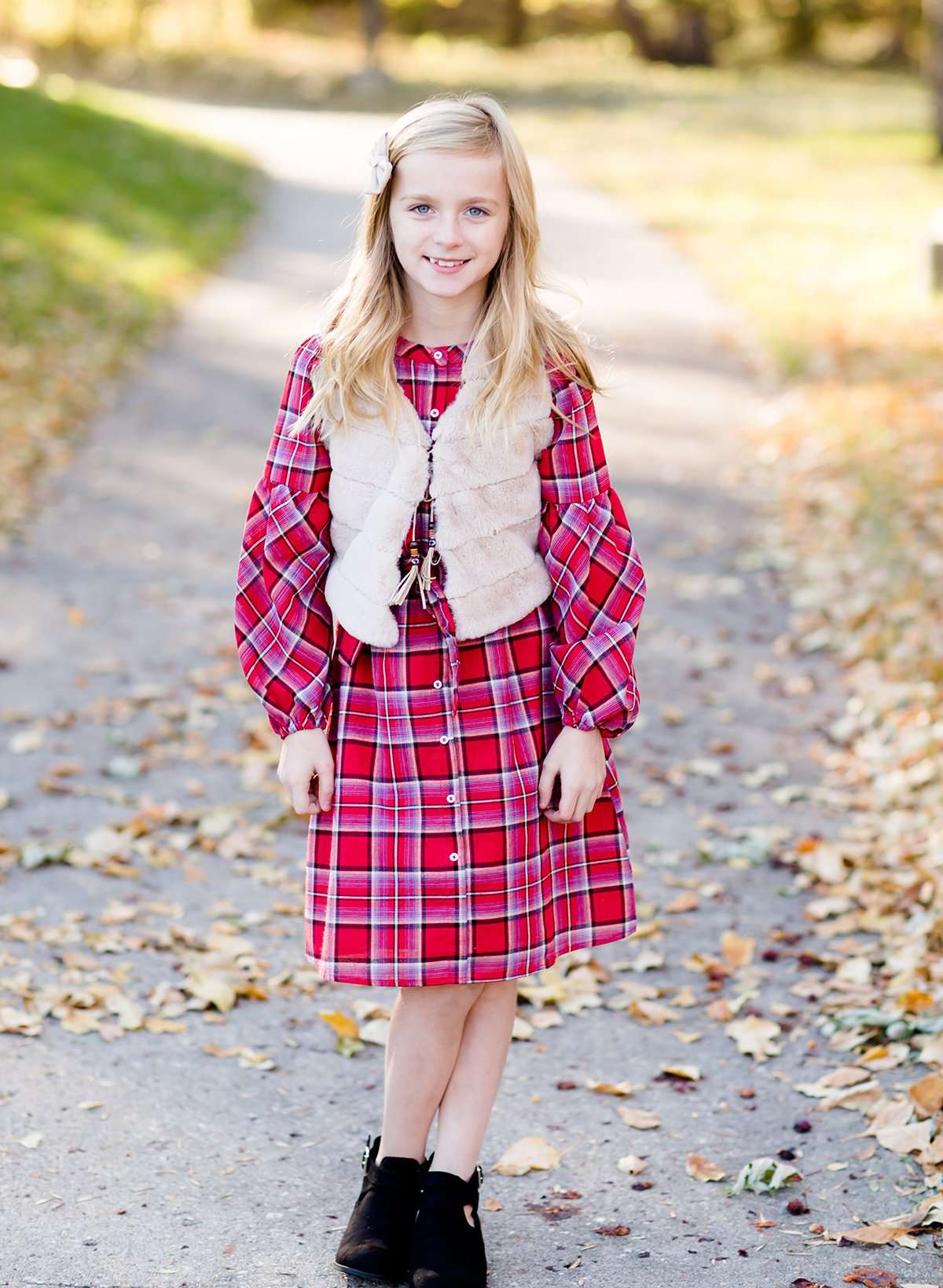 Young girl wearing a cream colored faux fur vest. It is a modest layering vest that also features beaded detail