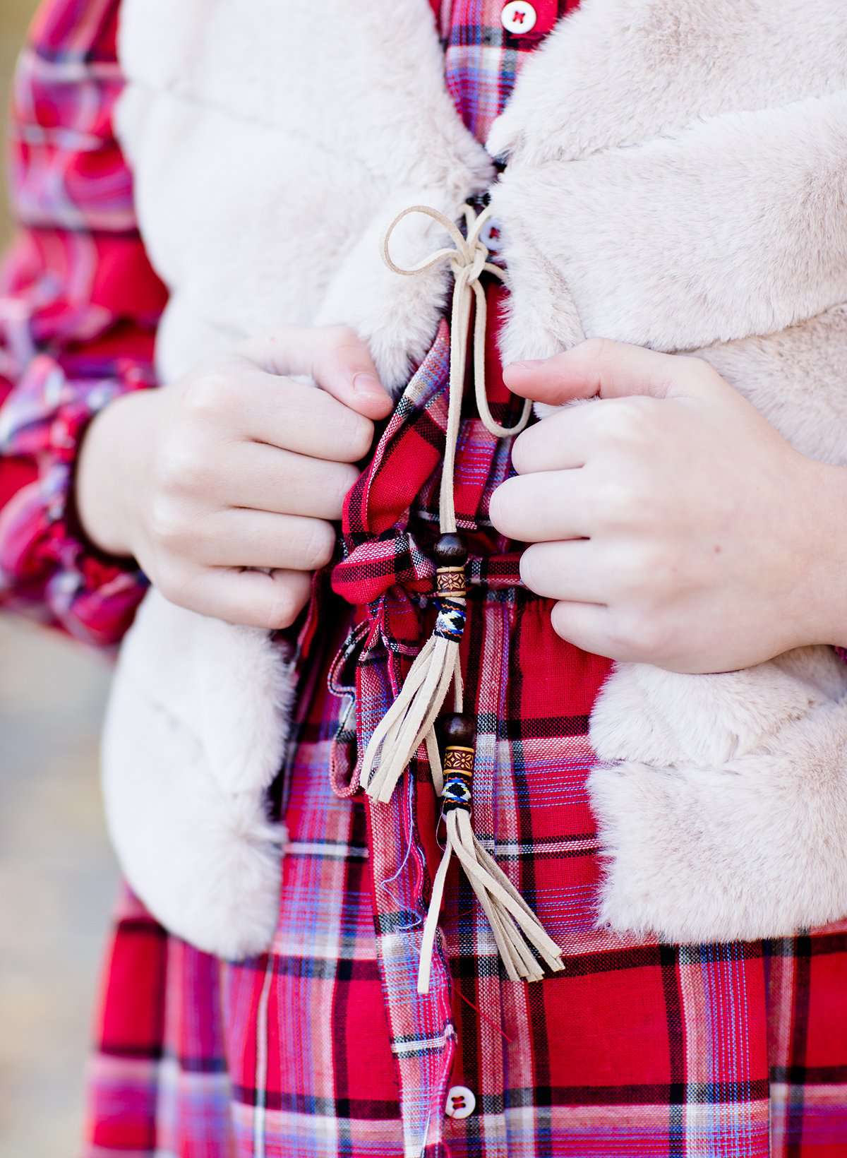 Young girl wearing a cream colored faux fur vest. It is a modest layering vest that also features beaded detail