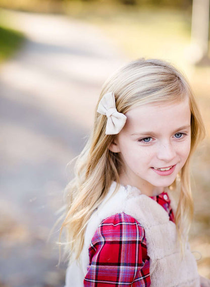 Young girl wearing a cream colored faux fur vest. It is a modest layering vest that also features beaded detail