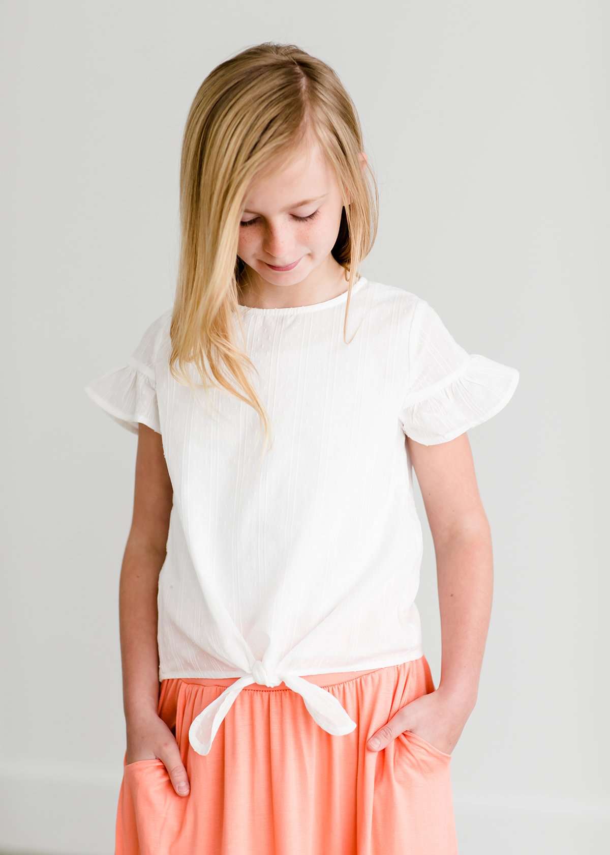 Girl wearing a modest ivory colored tie front top with flutter sleeves