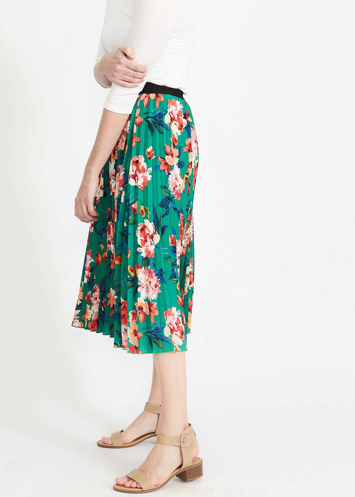 Woman wearing an emerald green floral stretchy pleated swing skirt with dress shoes and a white lace top