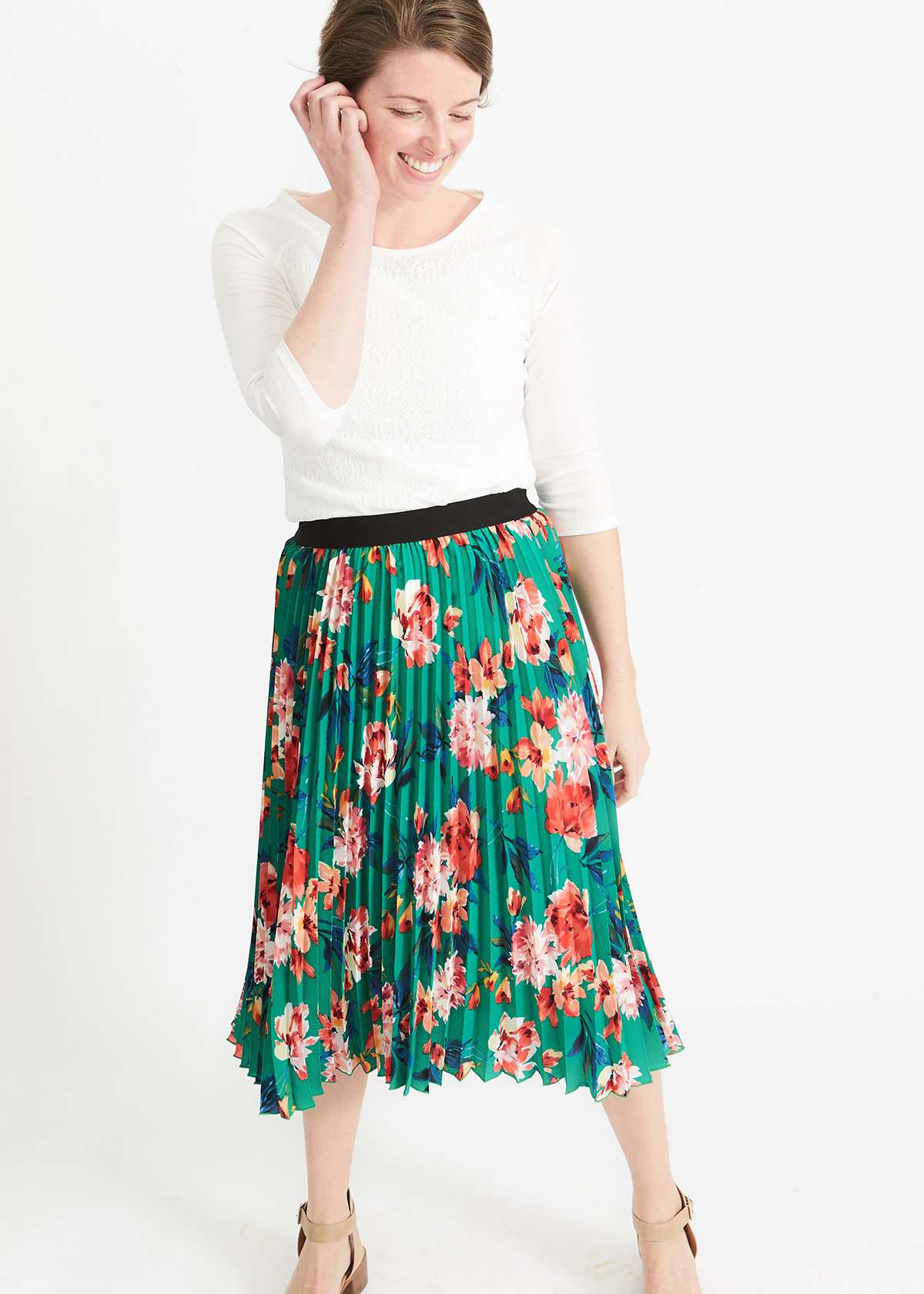 Woman wearing an emerald green floral stretchy pleated swing skirt with dress shoes and a white lace top