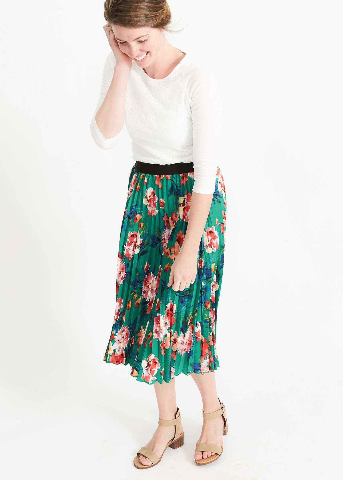 Woman wearing an emerald green floral stretchy pleated swing skirt with dress shoes and a white lace top