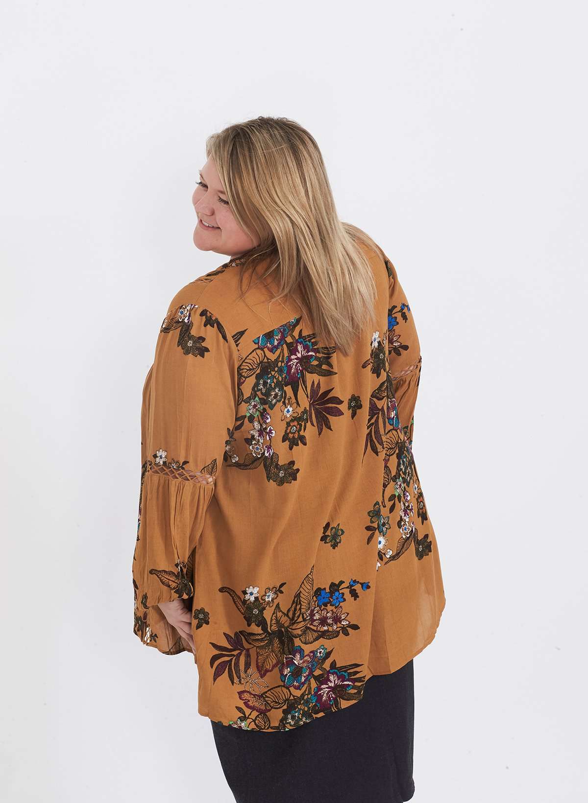 Plus size woman wearing a mustard floral lattice trim style tunic. This top is paired with a below the knee black skirt and leggings.