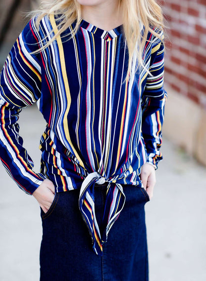 Young girl wearing a multi colored striped dolman top with a front tie. Colors in this top are navy, yellow, red, purple, green and white!