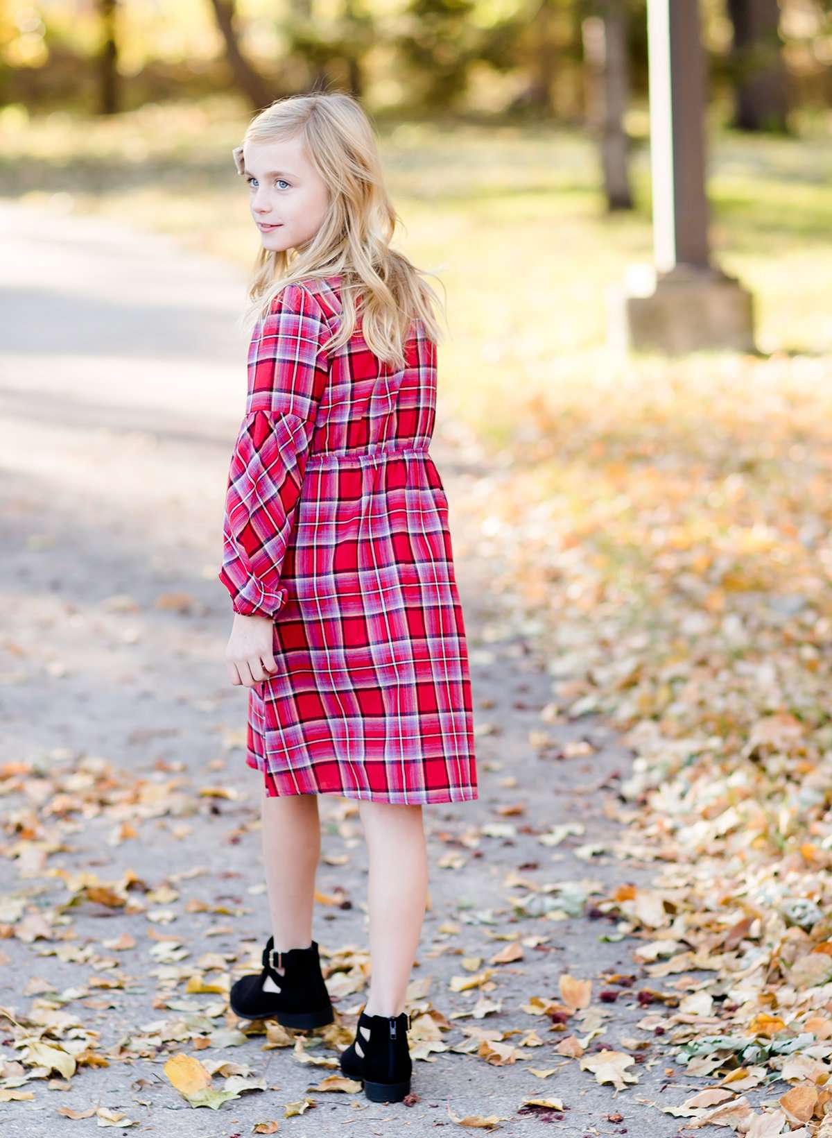 Young girl wearing a modest red plaid midi dress with balloon style sleeves. This dress also features a self tie fabric waist and is lined.