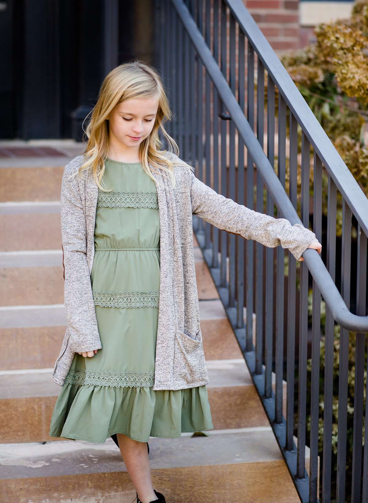 Young girl wearing a sage colored ruffle dress with lace trim on the tiers of the ruffles.