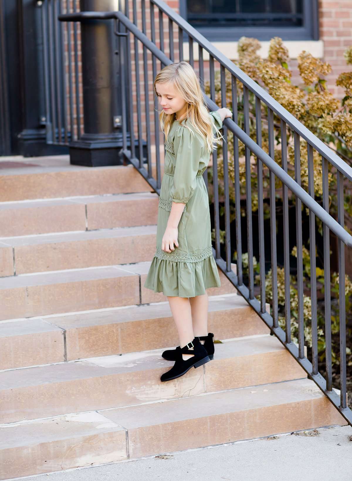 Young girl wearing a sage colored ruffle dress with lace trim on the tiers of the ruffles.