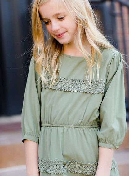 Young girl wearing a sage colored ruffle dress with lace trim on the tiers of the ruffles.